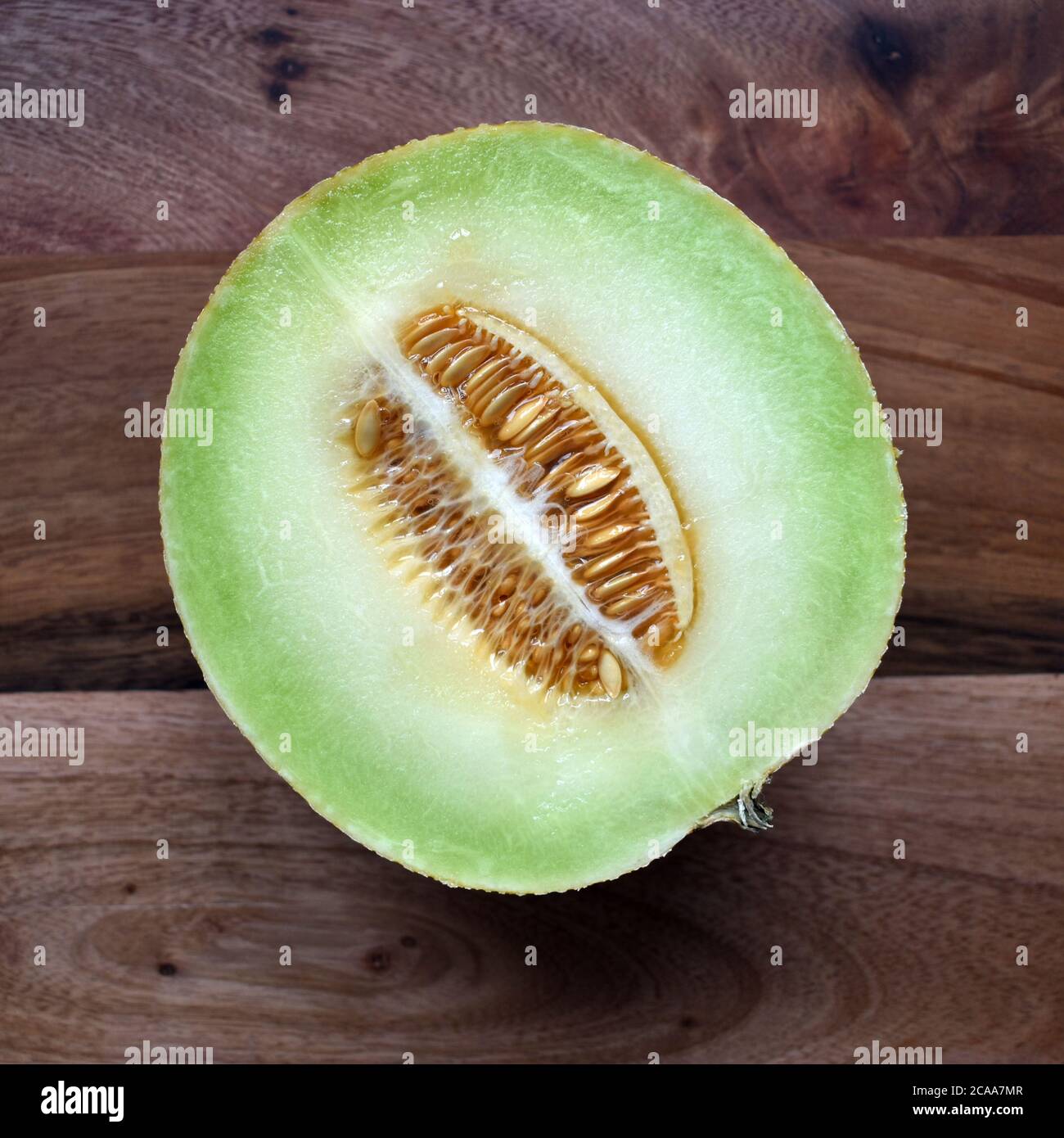 Fresh Galia Melon fruit halved photograph showing seeds and flesh on a wood background under natural light. Appetising, appealing, inviting  fruit Stock Photo