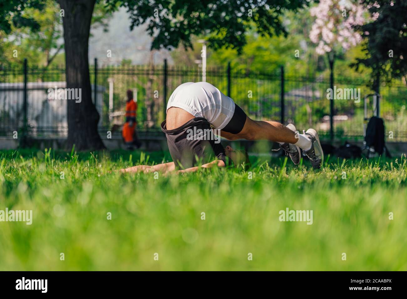 Young sporty handsome man practicing yoga in the park and doing the plow pose. Stock Photo