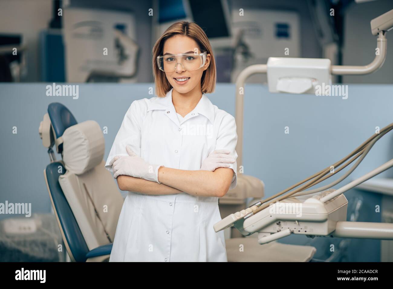 portrait of female dentist in white doctor's uniform standing in office near equipment and look at camera. Medicine, dentist, orthodontic concept Stock Photo