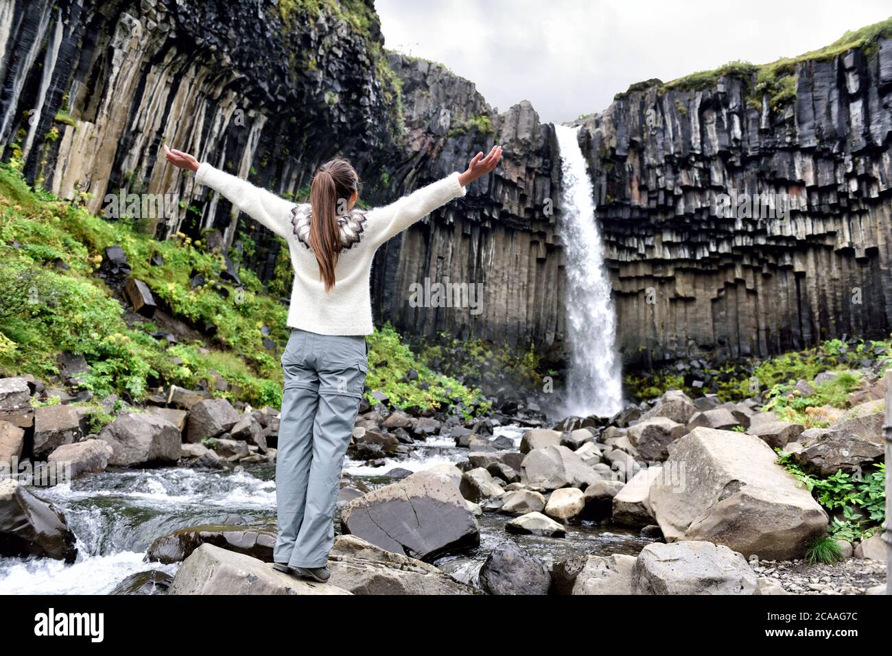 Iceland. Woman enjoying majestic Svartifoss waterfall. Female is visiting famous tourist attraction of Iceland. Spectacular natural landmark on Stock Photo