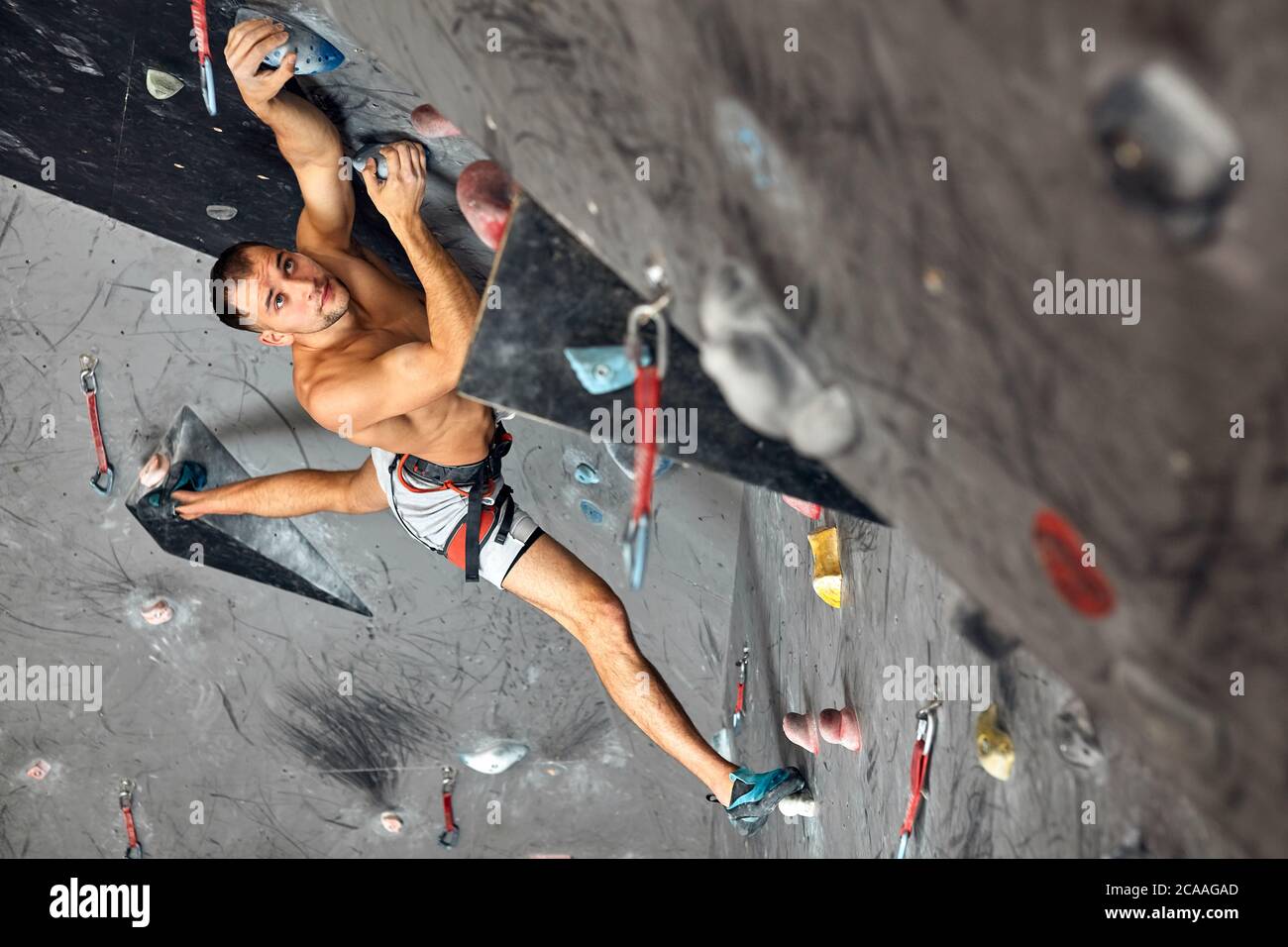 Athletic shirtless man hanging on hands at an indoor climbing centre