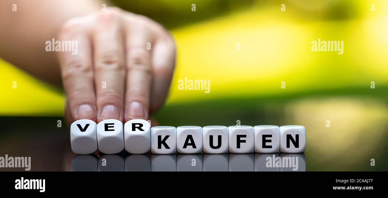 Hand turns dice and changes the German word 'kaufen' (buy) to 'verkaufen' (sell). Stock Photo