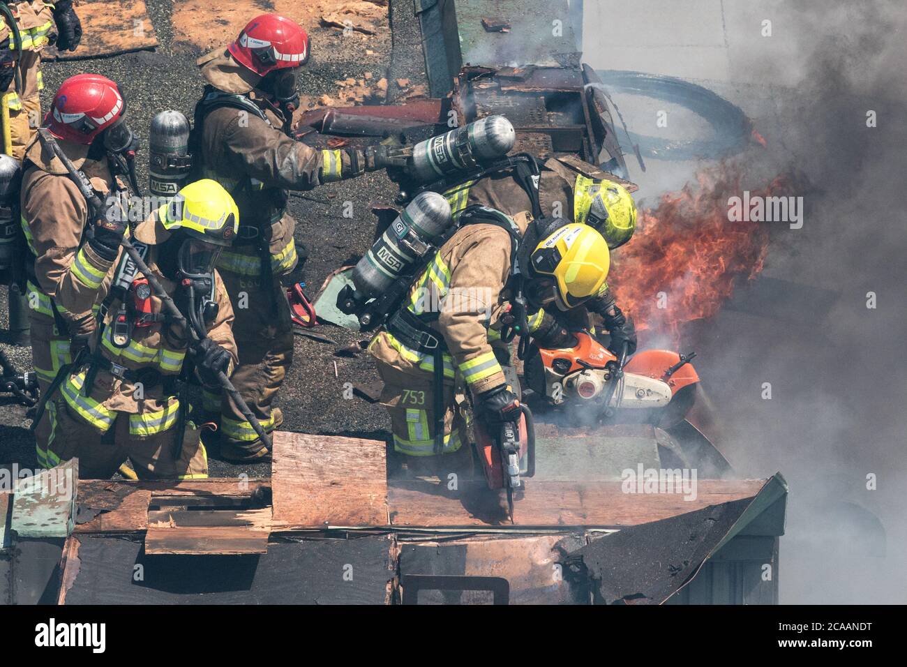 Firefighter using axe and pike polce on involved roof on fire Stock Photo