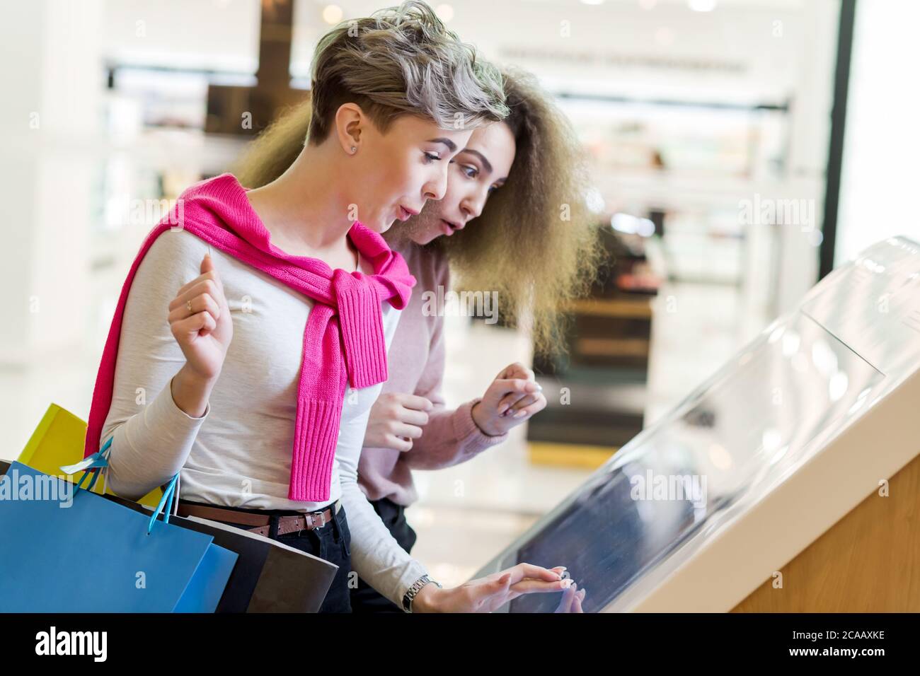 Two female customers standing near electronic information desk looking for boutique or shop location in the big mall Stock Photo