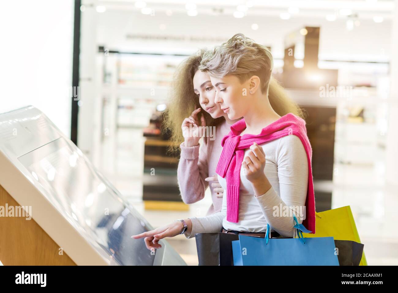 Two female customers standing near electronic information desk looking for boutique or shop location in the big mall Stock Photo