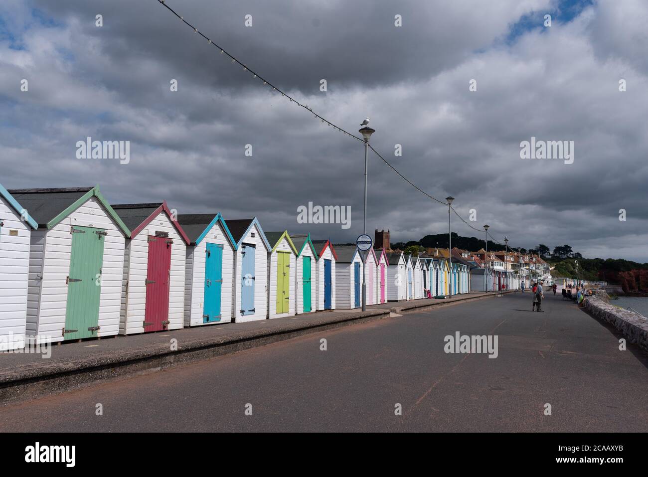 People sitting by Beach huts at Paignton enjoying the sun between the clouds on a typical British summer weather Stock Photo
