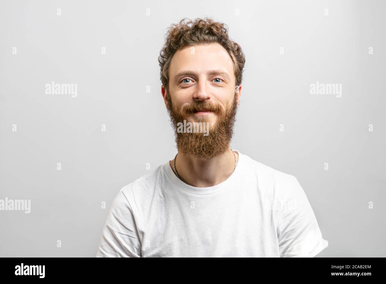 Portrait of young handsome softie, good-looking kind hipster man with beard smiling and looking at camera over white background. Stock Photo