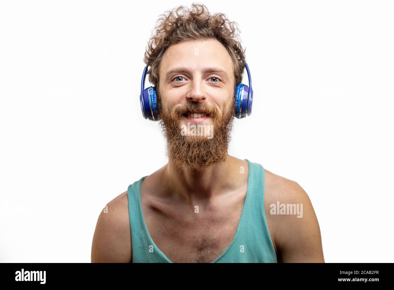 Portrait of young handsome softie, good-looking kind hipster man with headphones smiling and looking at camera over white background with copyspace. Stock Photo