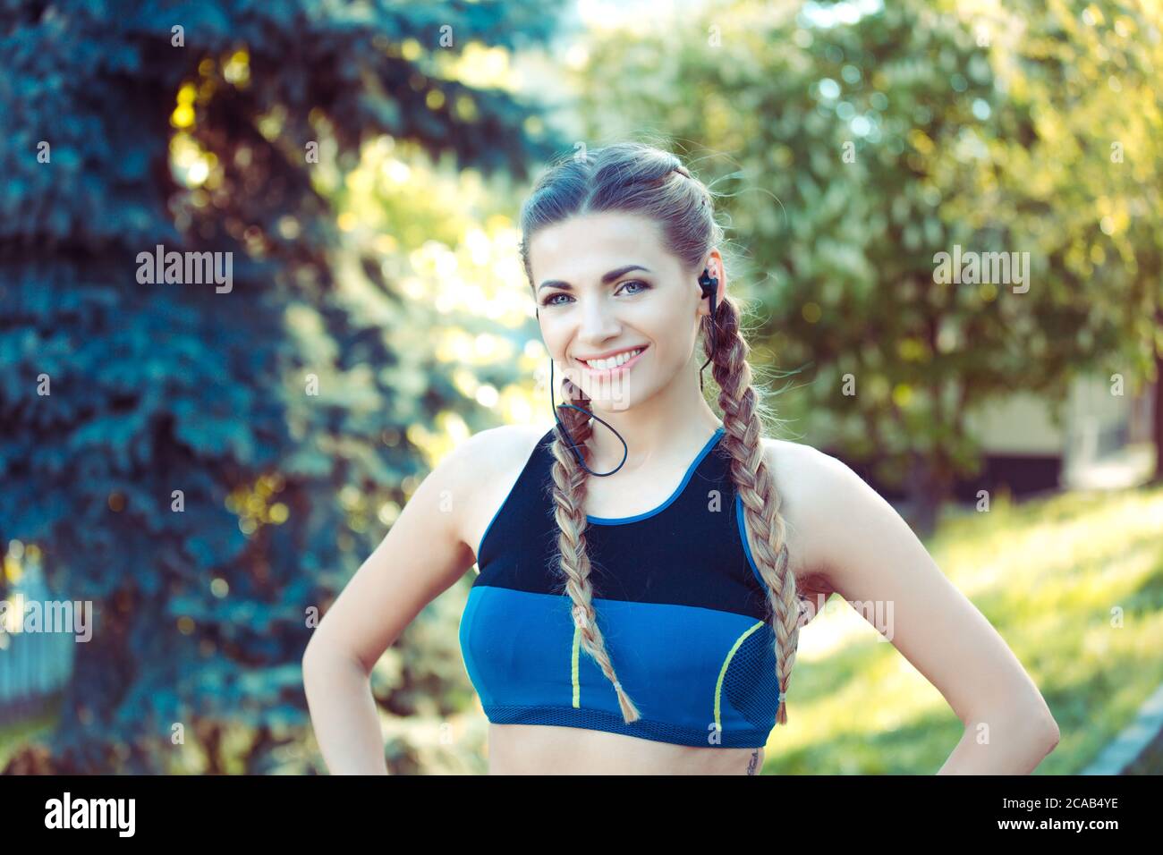 Young fit athletic woman in top and headphones standing in park and looking at camera Stock Photo