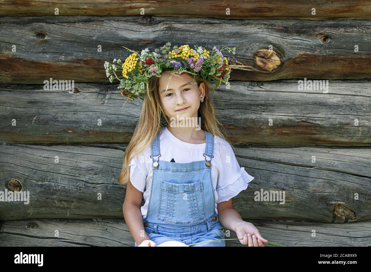 Cute teenage girl in flower wreath. Background wall of logs. Summer portrait of a happy girl Stock Photo
