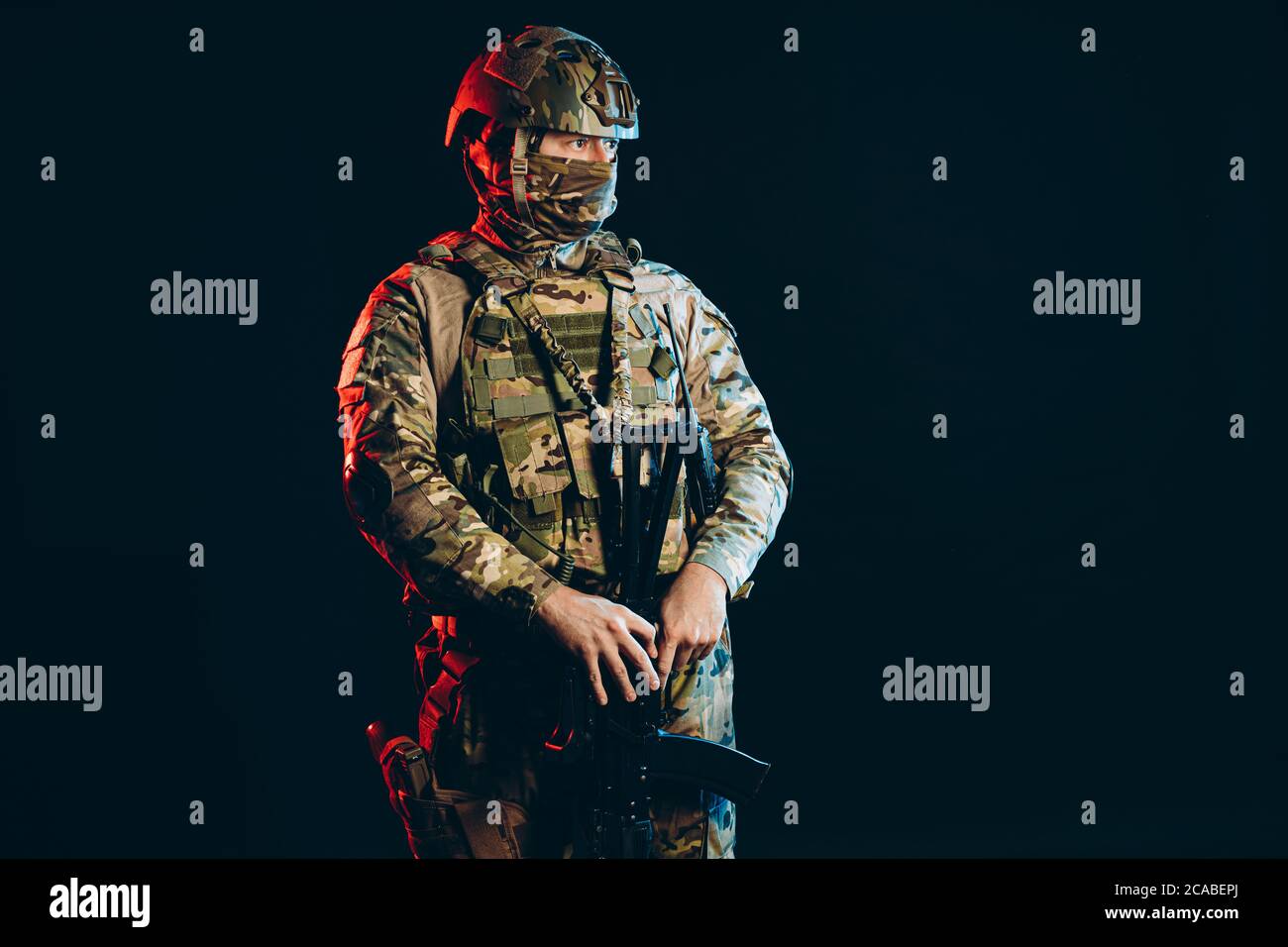 young serious soldier in green army clothes stand looking side at enemy, isolated over black background with UV rays Stock Photo