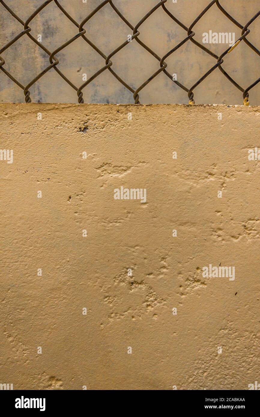 Close-up old iron wire fence vintage net on the background of concrete beige painted wall. Vertical format. Copy space ideal for use in the design or Stock Photo