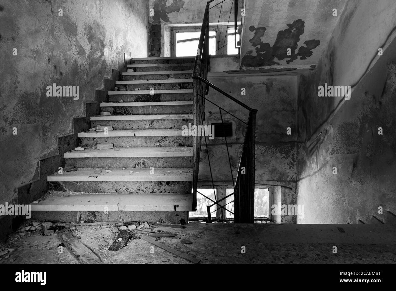 Black and white image of stairway covered in rubble, mold and stains on the walls. Abandoned building located on Monte Grappa (Veneto, Italy) Stock Photo