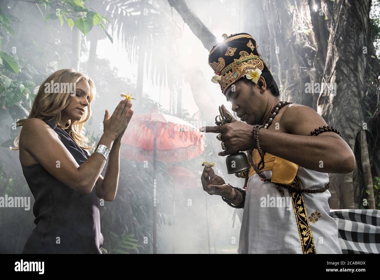 Asia, Indonesia, Bali, young, beautiful Caucasian woman wearing smart casual clothing, enjoying a local cultural experience, being blessed by a Baline Stock Photo