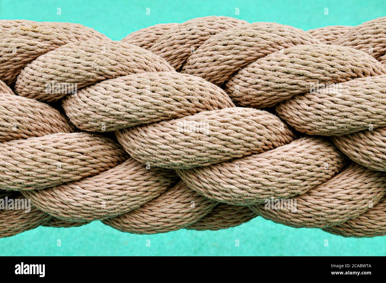 A close up image of a thick industrial rope, with many rope lengths coiled together in a spiral, against a blue background. Stock Photo