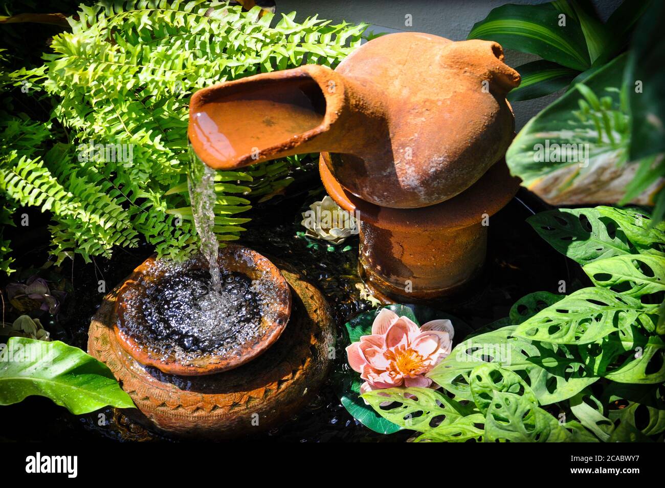 Cascading terracotta garden feature in a small courtyard patio setting, with lush tropical greenery, ferns and water lillies. Stock Photo