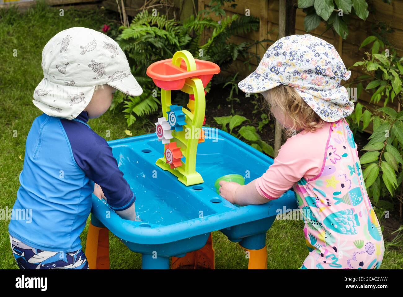 Authentic image of toddler twins toddlers pre-school young children kids playing in water with toys outdoors in a garden in summer. England UK Britain Stock Photo