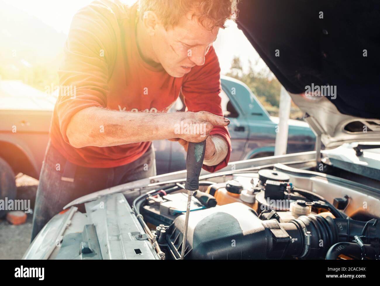 The concept of disability of people and their adaptation to life. A blond disabled man repairs a car, works with a screwdriver. There are no fingers o Stock Photo