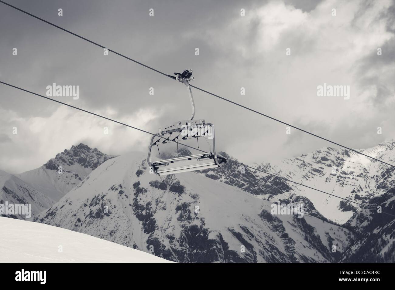 Sunlit chair lift, snowy ski slope, high winter mountains and cloudy ...