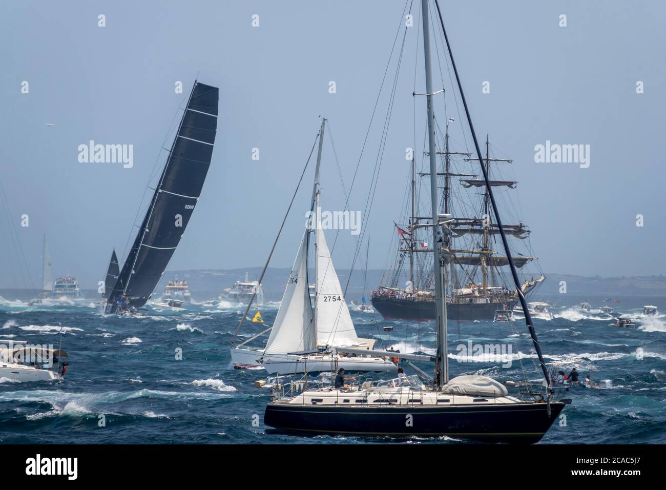 The organised chaos of the 2019 Sydney to Hobart yacht race start passing Sydney Heads, with maxi yacht Black Jack passing the Tall Ship 'James Craig' Stock Photo