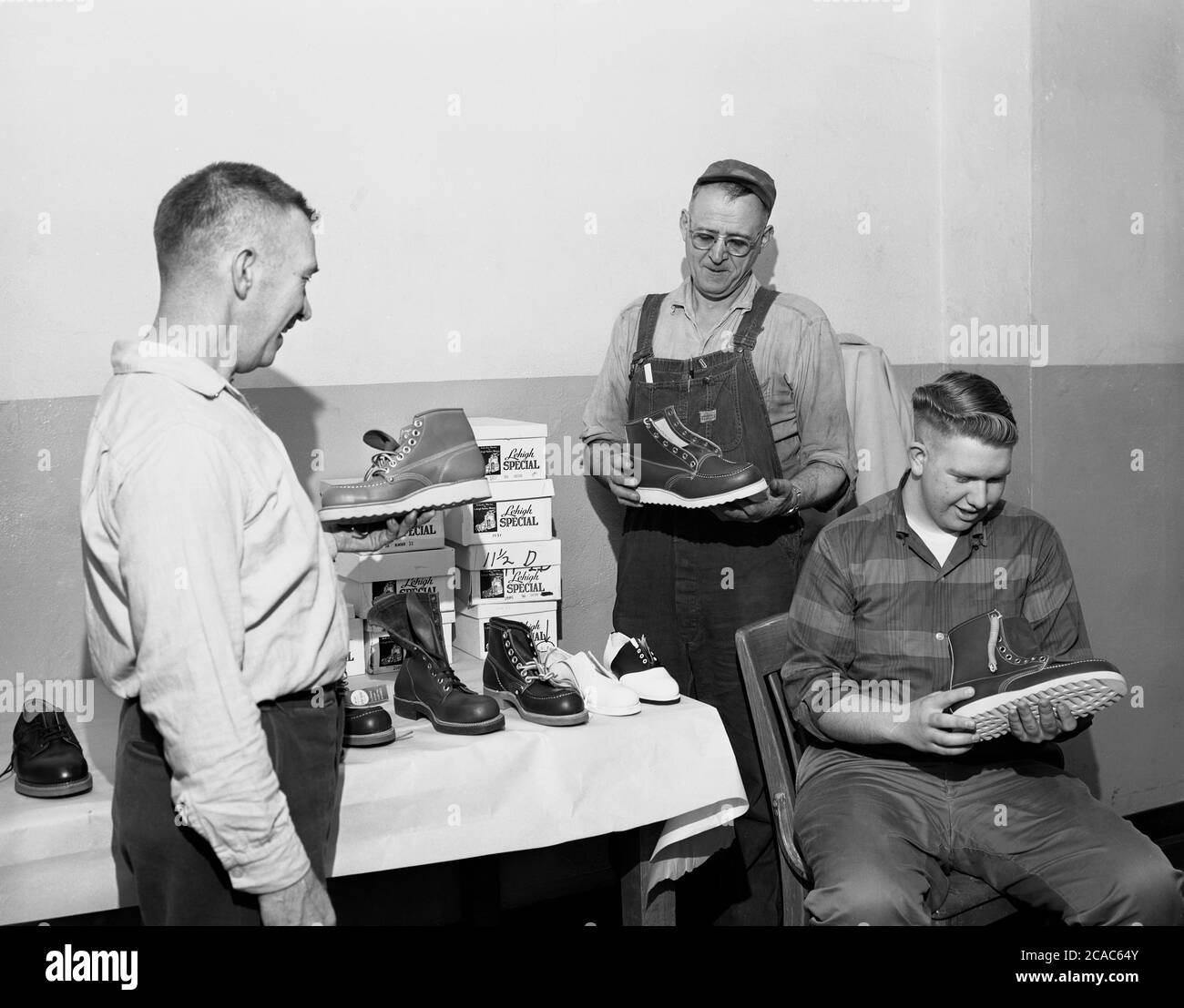 circa1940s, historical, two workmen looking at a range of new lightweight leather-made industrial safety work boots, with the store owner standing by the display, Midwest, USA. Stock Photo