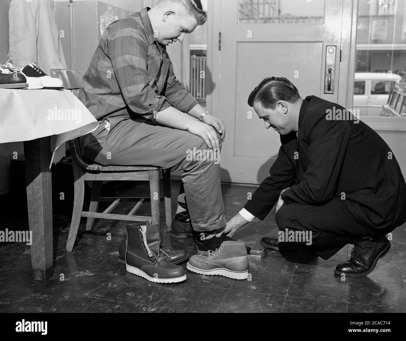 circa, 1940s, historical, inside a midwest American retail store, a young man sitton on a chair having his foot measured by a salesman, for a pair of new lightweight industrial leather safety work boots, USA. Stock Photo