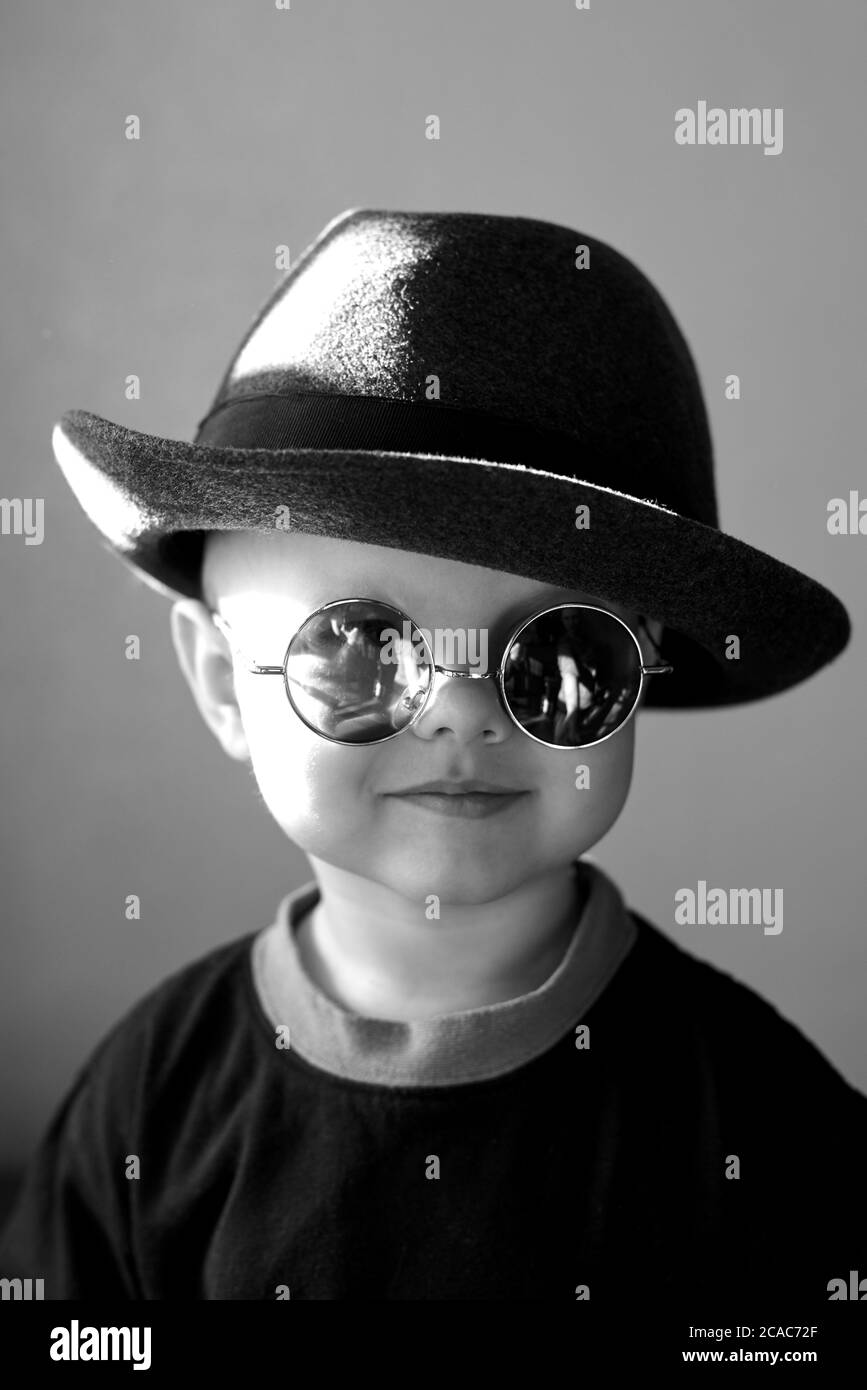 Portrait of a little cute funny boy in a retro hat and round glasses, black and white photo