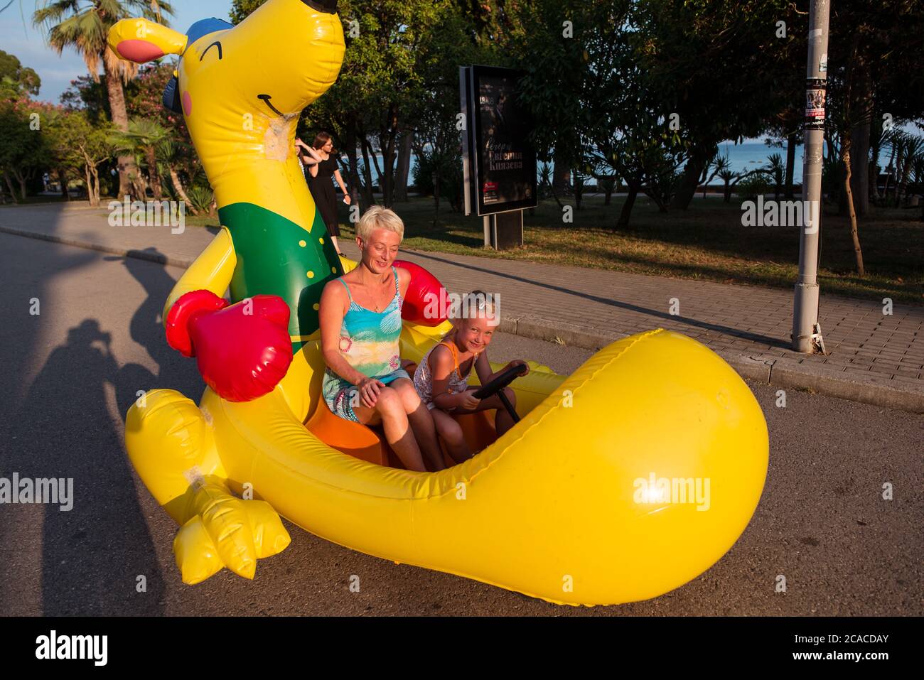 Sukhumi / Abkhazia - August 2, 2019: Russian mother and daughter tourists riding in toy vehicle simulating huge yellow plastic doll Stock Photo