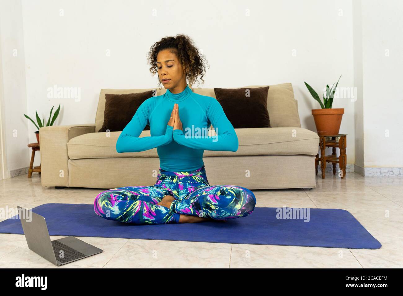 Brazilian black young woman training yoga at home with laptop in living room. Exercising on a mat. Stock Photo