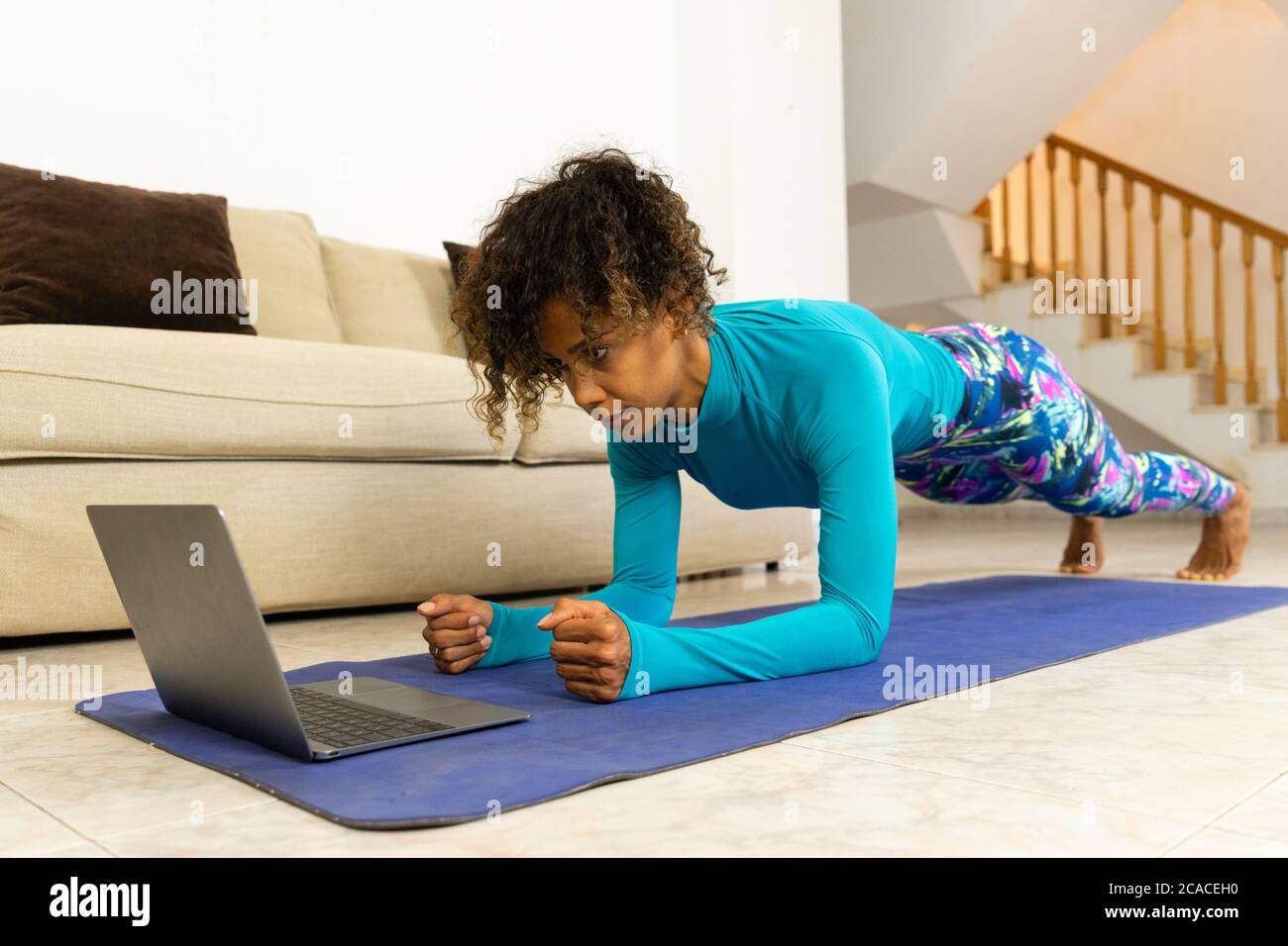 Brazilian black young woman training yoga at home with laptop in living room. Exercising on a mat. Stock Photo
