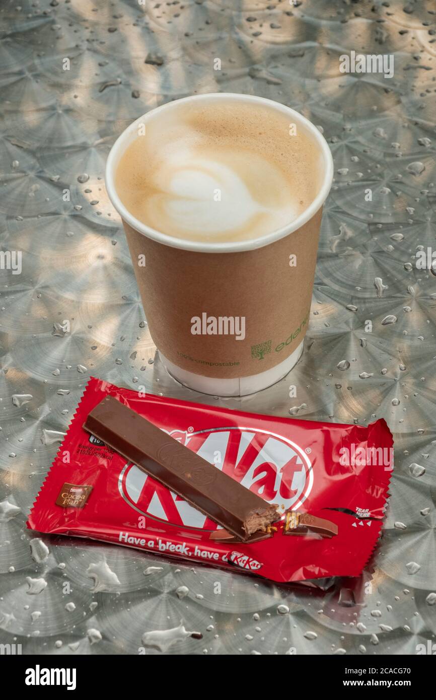 An empty KitKat wrapper on a wet table with a paper cup of latte coffee