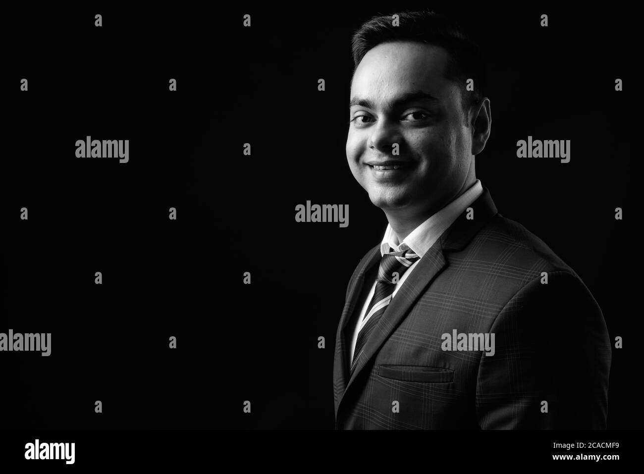 Portrait of happy young handsome Indian businessman in black and white Stock Photo