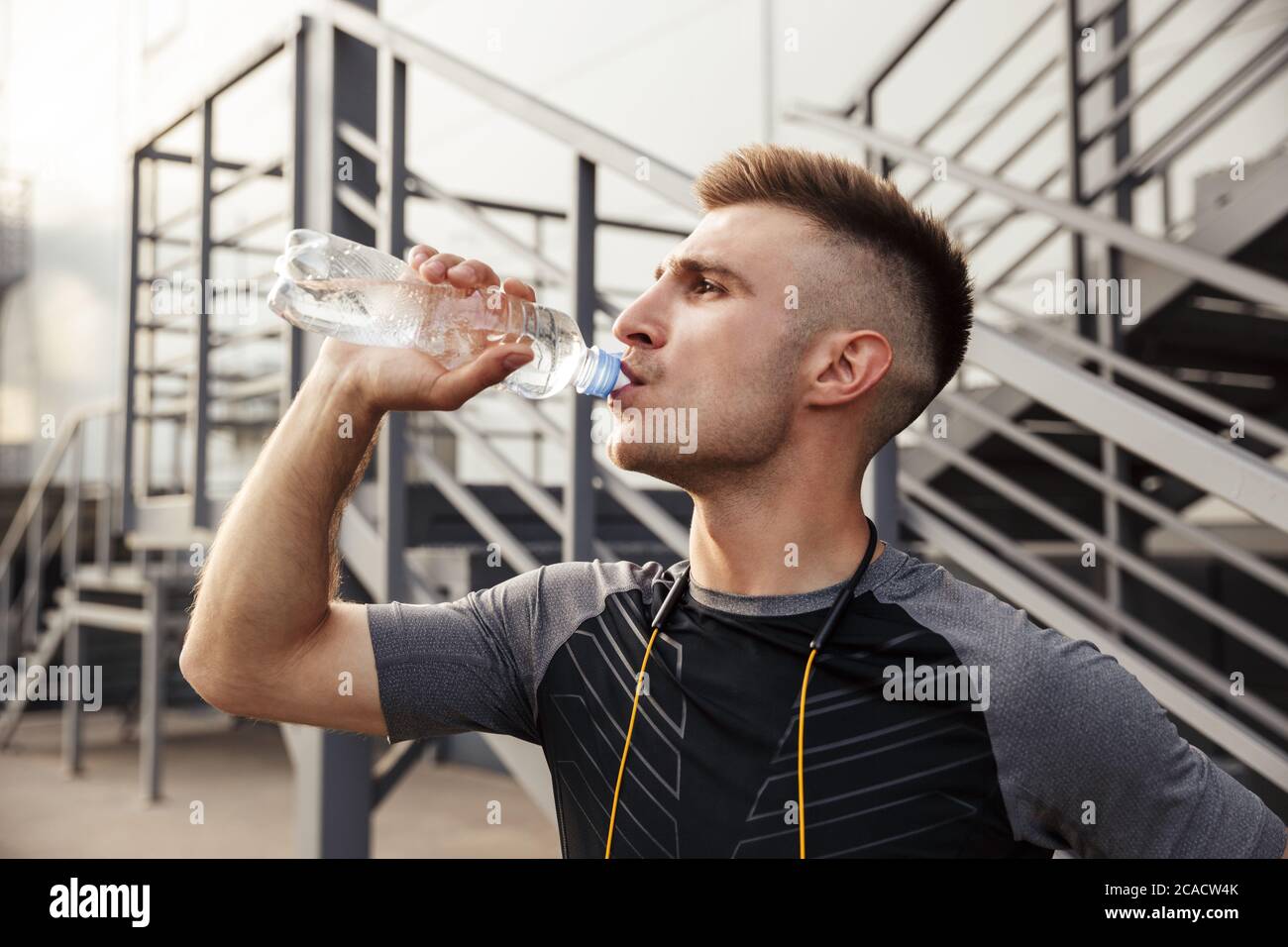 Image of unshaven caucasian sportsman drinking water while working out