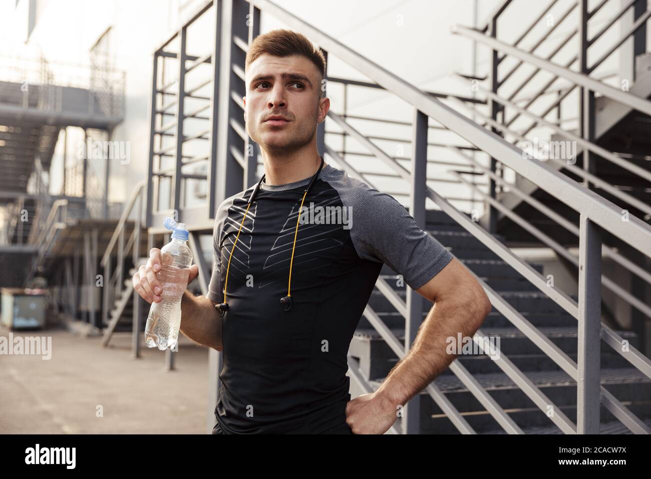 Image of unshaven caucasian sportsman drinking water while working out
