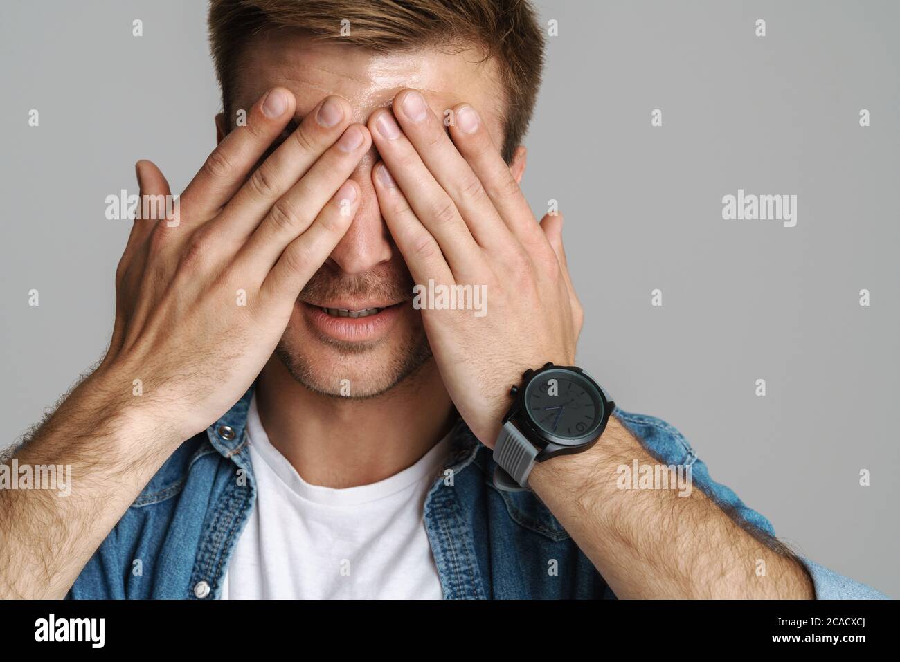 Portrait of calm unshaven man posing and covering his eyes isolated ...