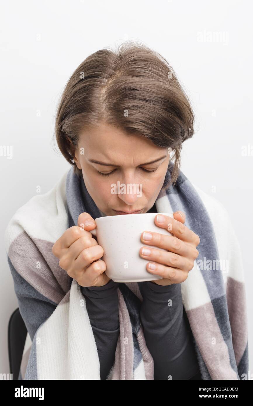 A sick, cold woman drinks tea wrapped in a blanket Stock Photo Alamy