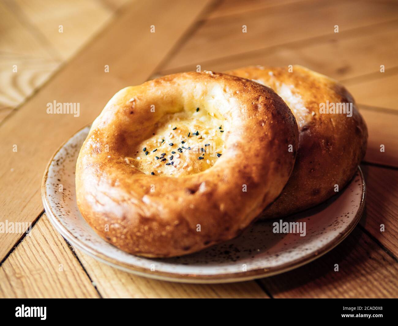 Tasty fresh tandoor bread on rustic wooden tabletop. Two tandoor flat bread cake with black sesame seeds on yellow wooden table background. National asian meal and food Stock Photo