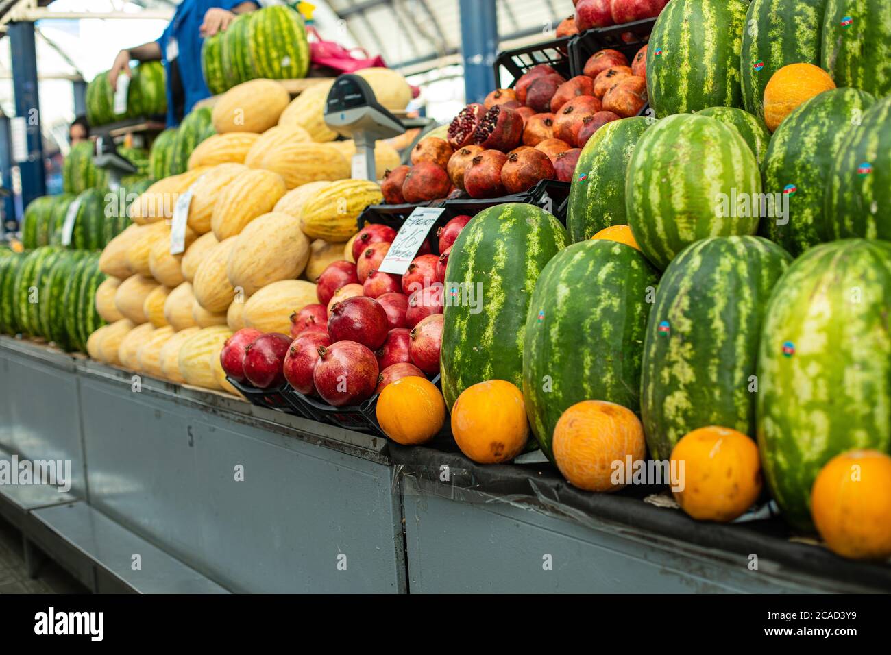 Lots of large green watermelons standing next to oranges and other fruits on the supermarket shelf Stock Photo