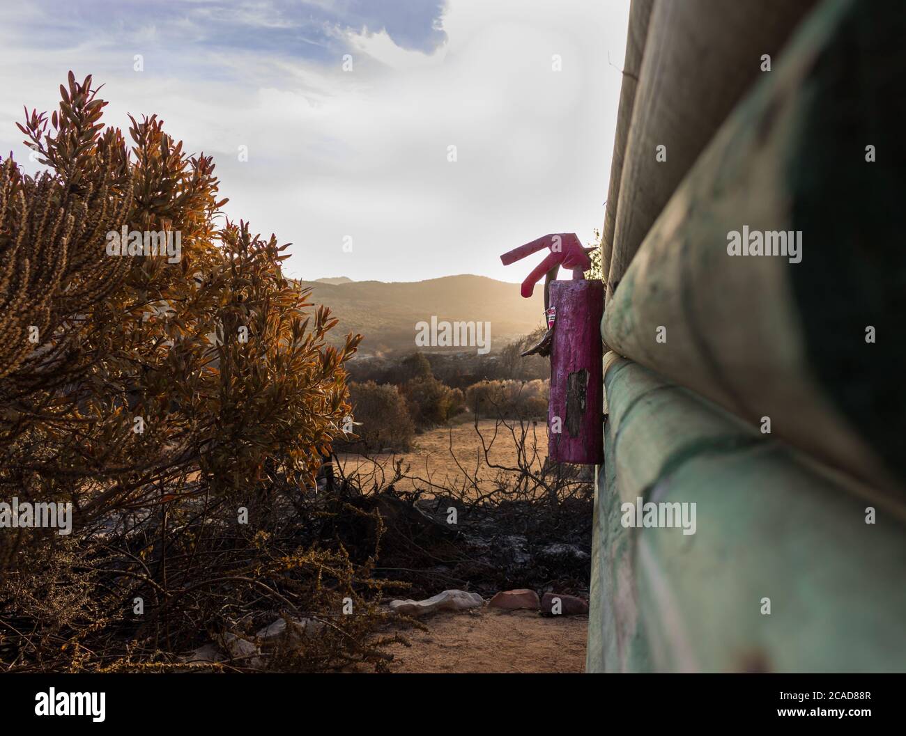 Burnt red Fire extinguisher hanging on side of building after a fire