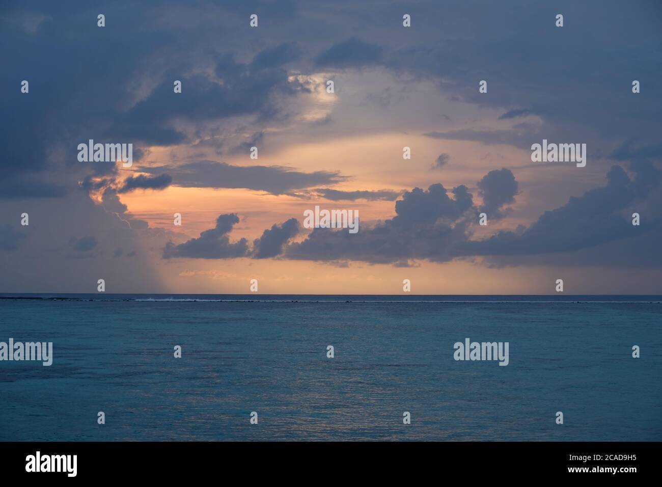 orange sunrise in cloudy blue sky of maldives. Blue peaceful ocean waves on horizon Stock Photo