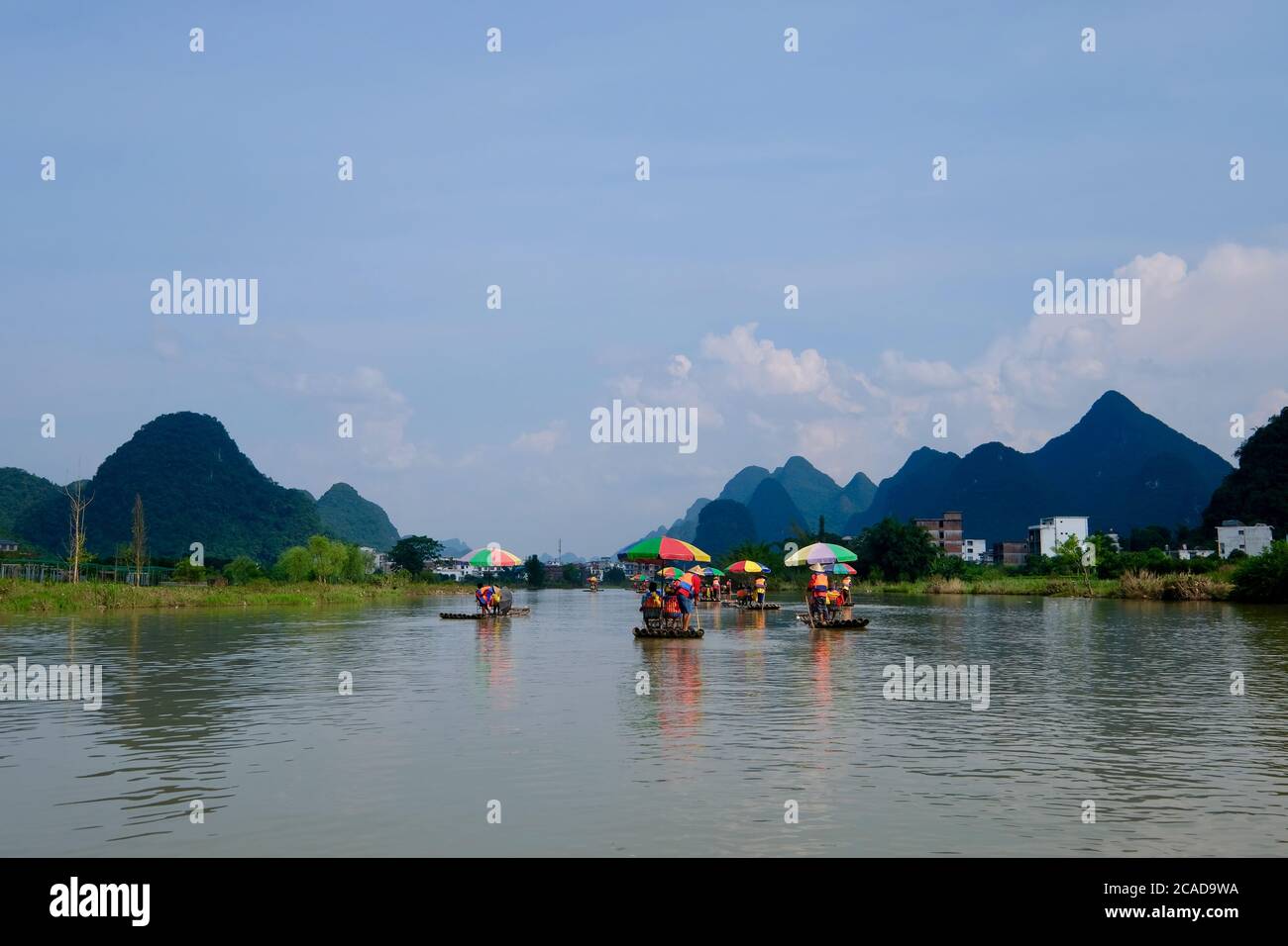 Several bamboo rafts floating on wide river. Blue mountains and blue sky with white clouds. In Yangshuo Guilin China. Karst landform Stock Photo