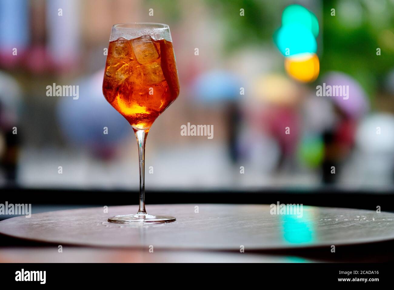 close up one wine glass of orange color cocktail on table, ice cubes and lemon slice inside. Defocused city lights Stock Photo