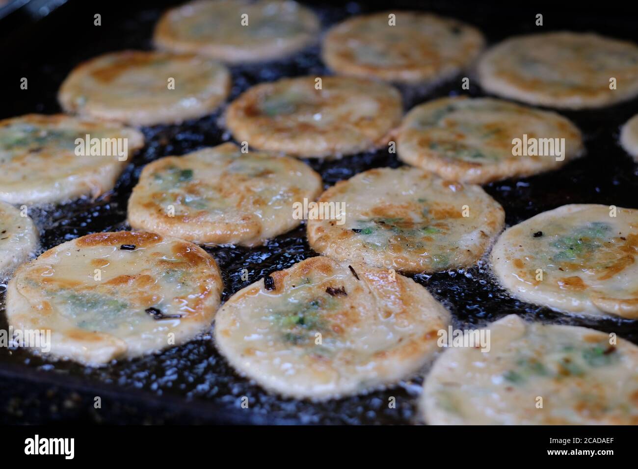 close up group of fried scallion pancakes in black pan. Boiling oil. Popular traditional Chinese folk food. Defocused Stock Photo
