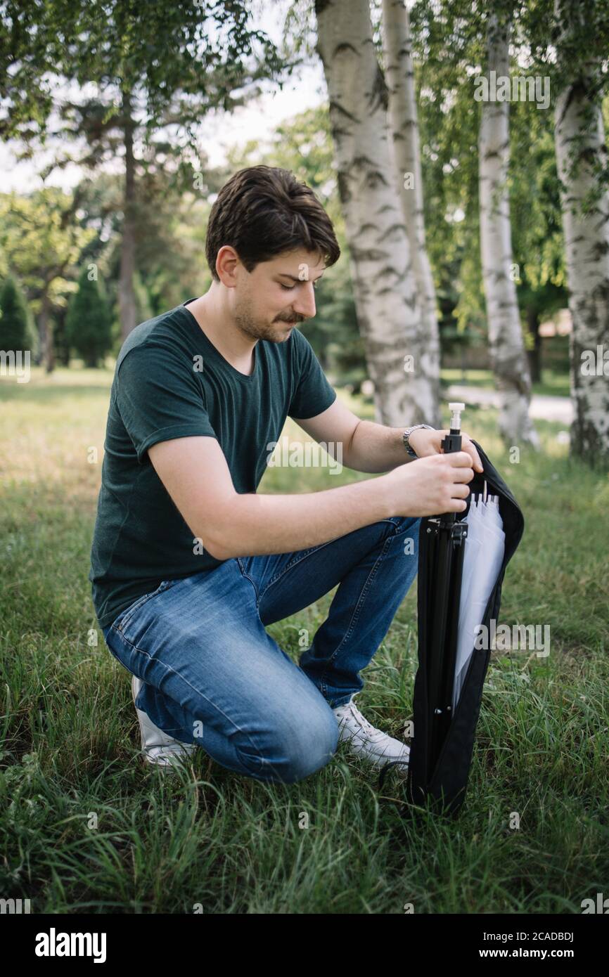 Young man holding camera stand while squatting in forest Stock Photo