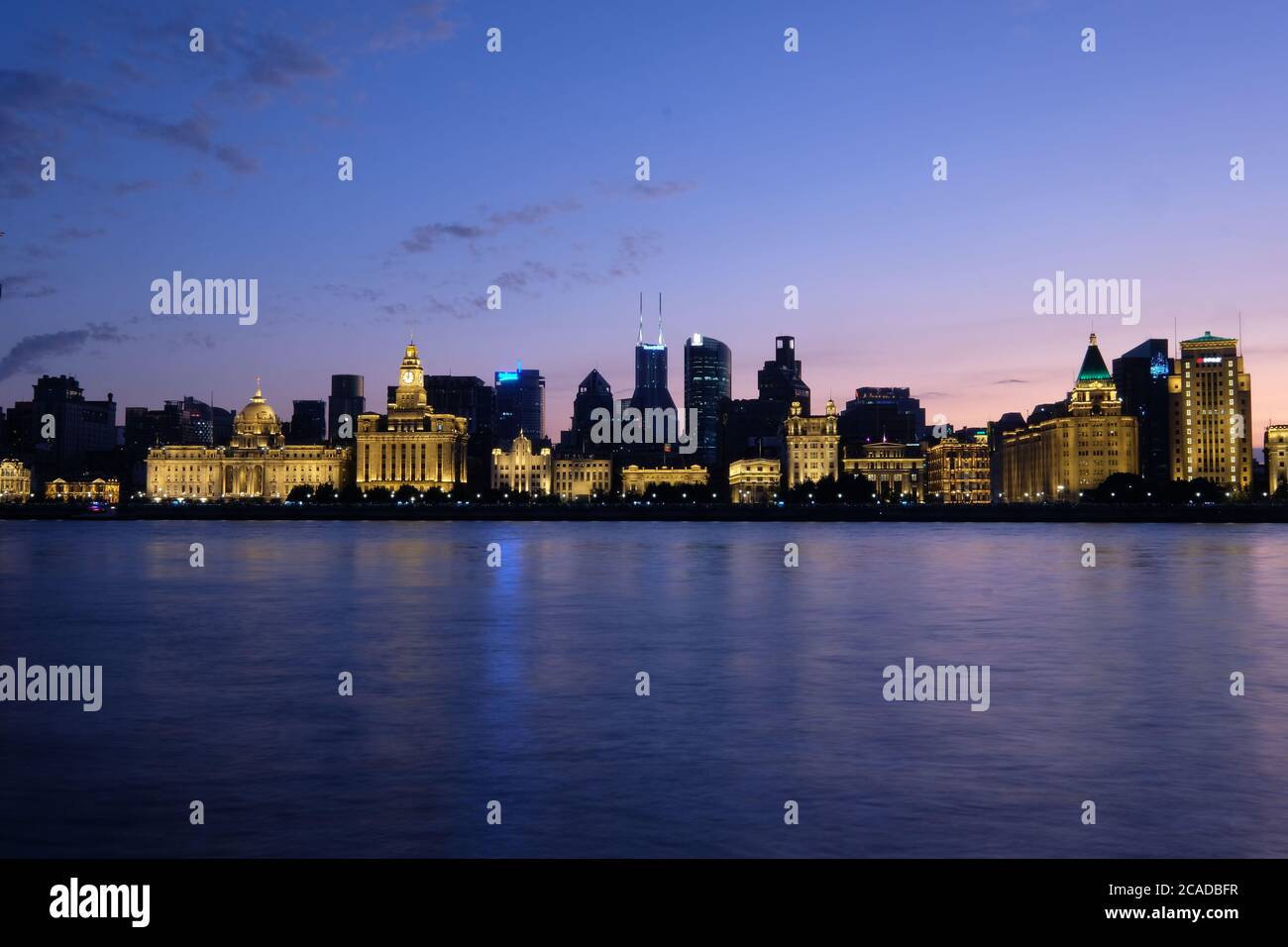 Sunset blue hour of The Bund in Shanghai. Golden illuminated western buildings on the bank of Huangpu River. Long exposure peaceful river. Wide angle Stock Photo