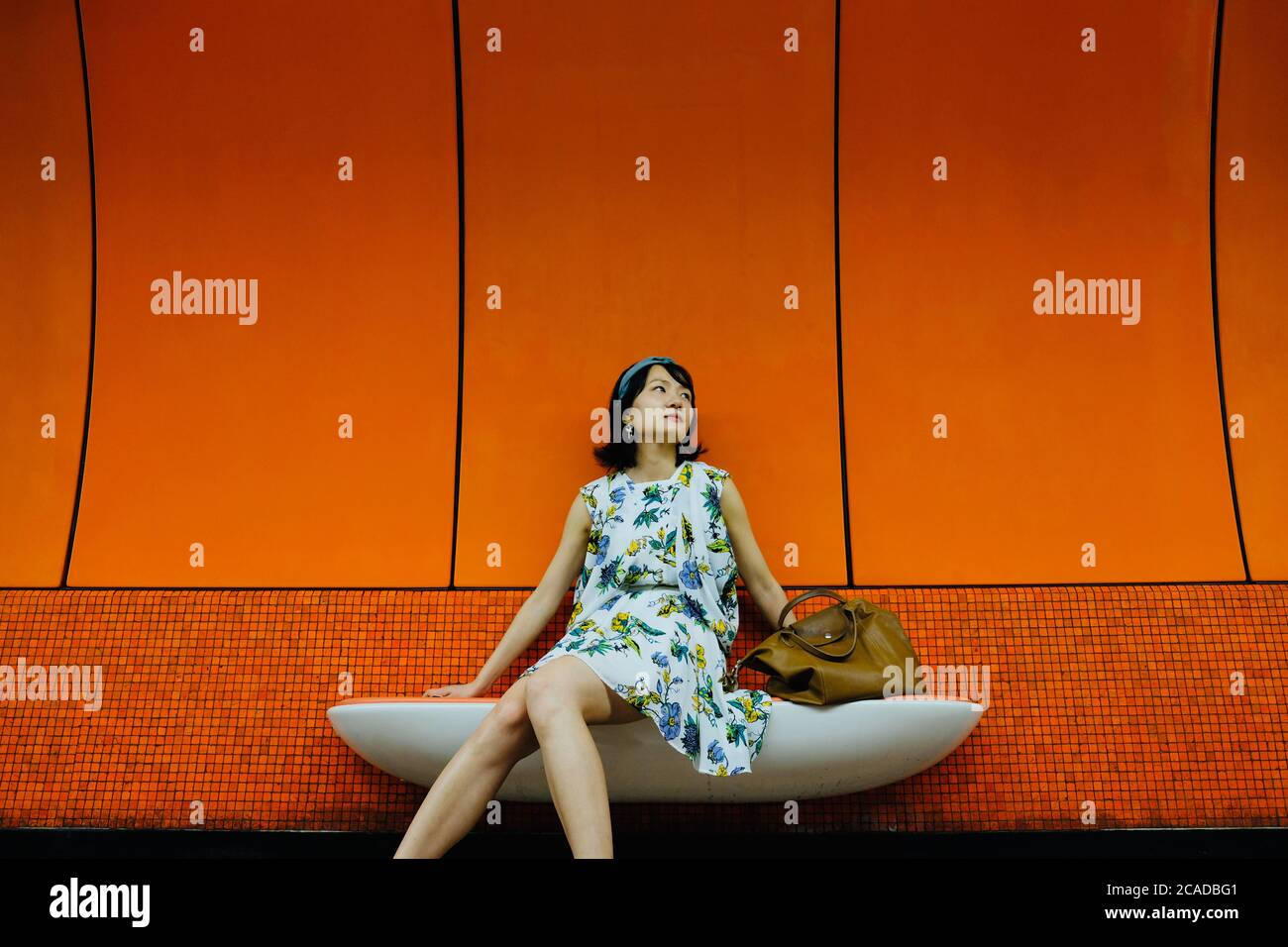 One elegant young Asian woman in floral dress with a handbag, sitting in subway station in Hongkong. Stock Photo