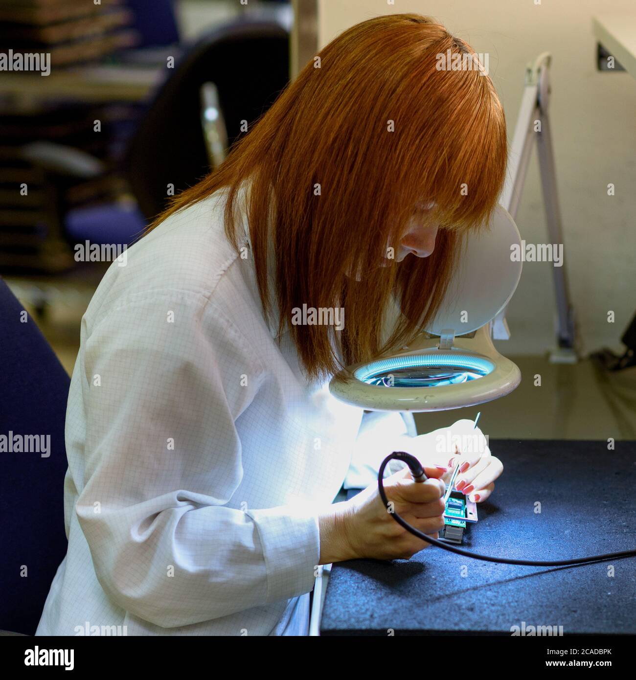 Woman Soldering a circuit board in her tech office.Close up of female engineer Middle-aged quality inspector is checking the item. Testing and fixing a circuit board. Stock Photo