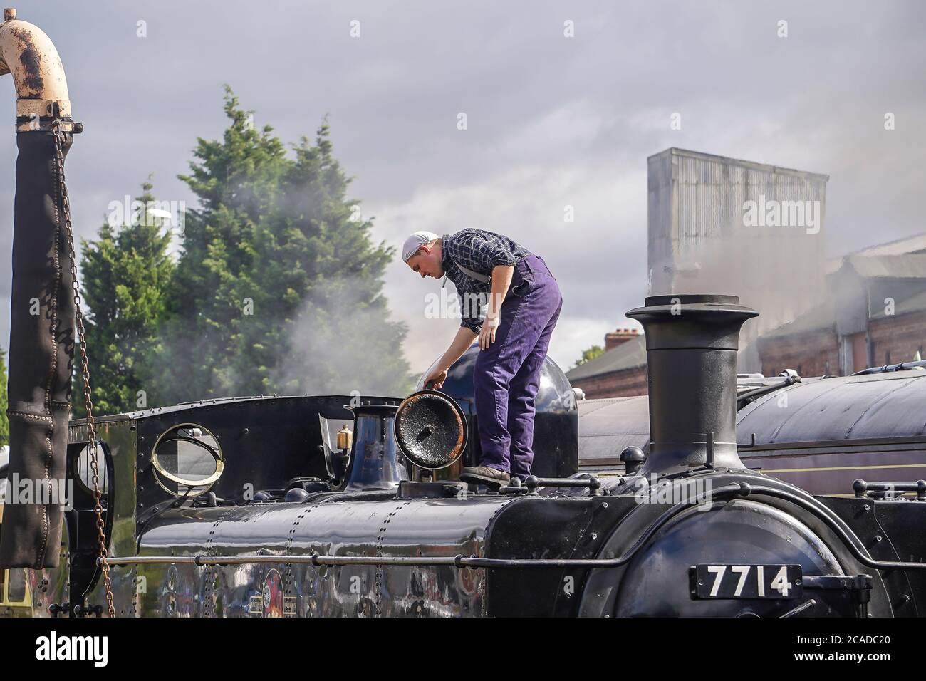 Steam locomotive fireman standing on vintage steam locomotive checking engine water levels, in sidings at heritage railway station, UK. Stock Photo