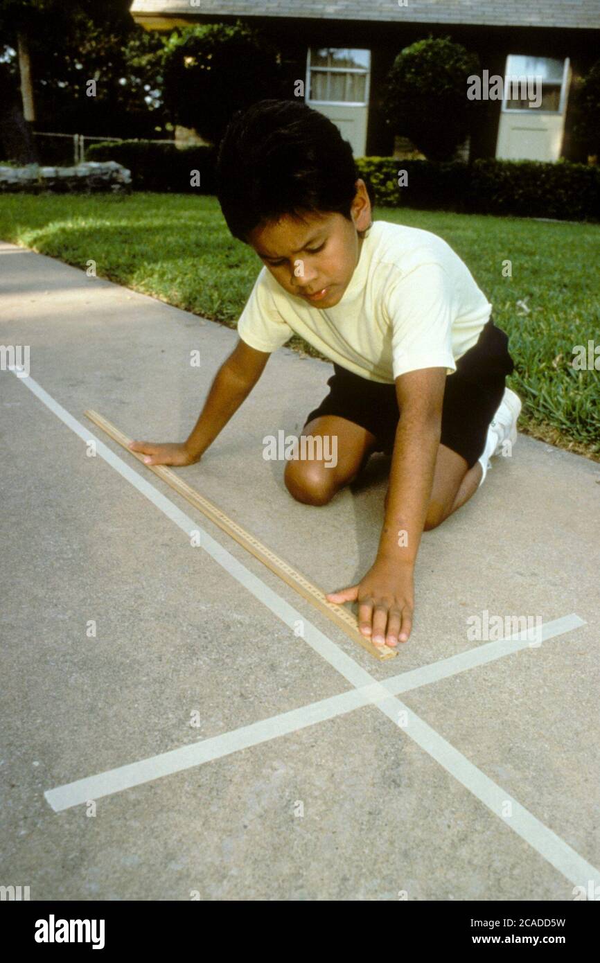 Hispanic young boy uses meter stick to measure tape on sidewalk. ©Bob