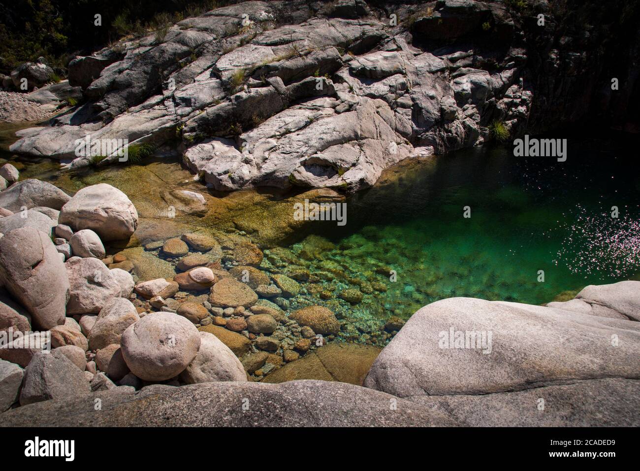 Crystal clear turquoise green water on mountain lake, showing round rocks on the bottom. Stock Photo